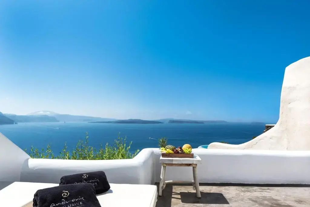 Sonnige Terrasse mit Liegestühlen, einem Beistelltisch mit Früchten und weiter Sicht auf das Meer.