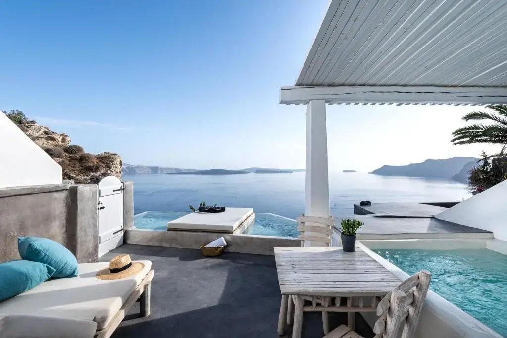 Überdachte Terrasse mit Holztisch, Sonnenliege und Blick auf das blaue Meer.