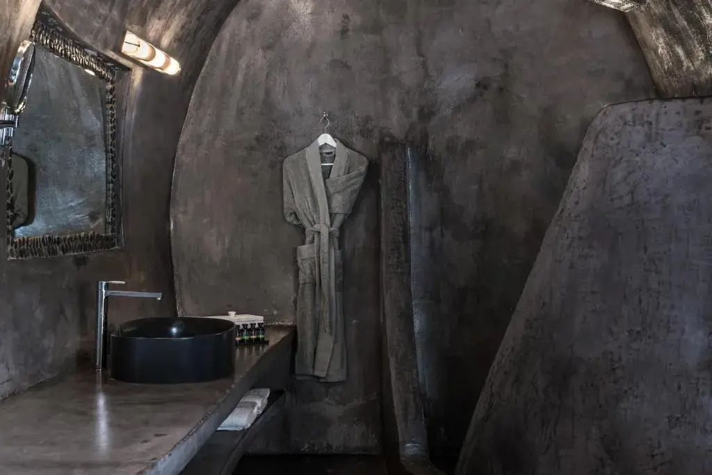 Badezimmer in Höhlenarchitektur mit dunklem Waschtisch und einem Bademantel.