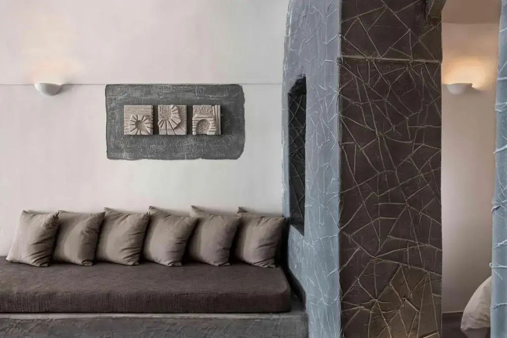 Sitzbank mit braunen Kissen neben einer strukturierten Wand und Reliefs aus Stein.