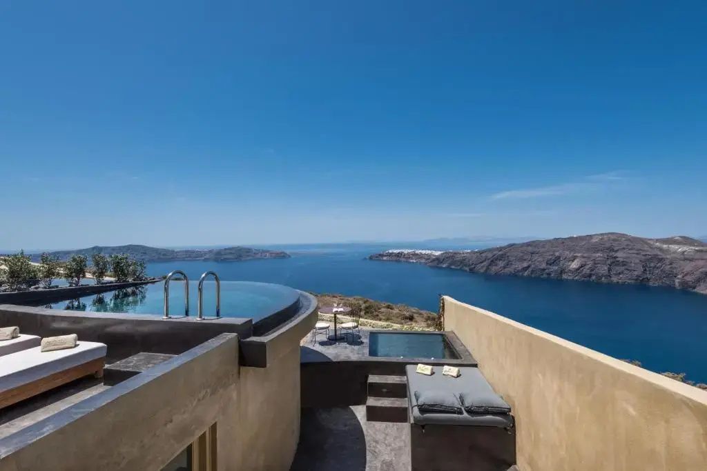 Terrasse mit Infinitypool, Liegebett und Weitblick auf das Meer und die Küste von Santorin.