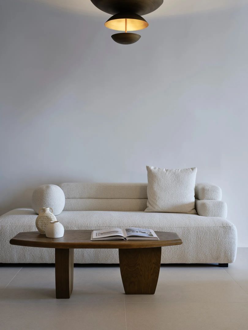 Helles Sofa aus Stoff mit einem hölzernen Couchtisch davor in einem schlichten Raum.