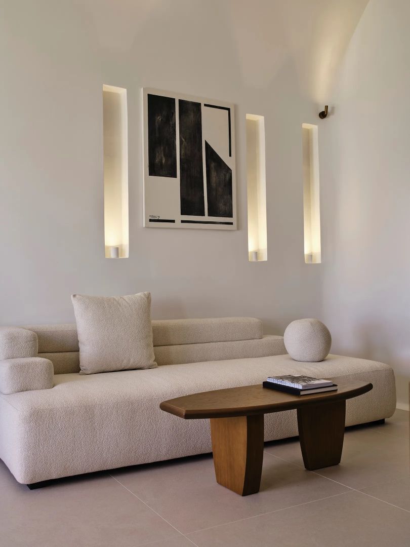 Helles Polstersofa mit Holz-Couchtisch vor einer Wand mit Wandbild und Lichtnischen.