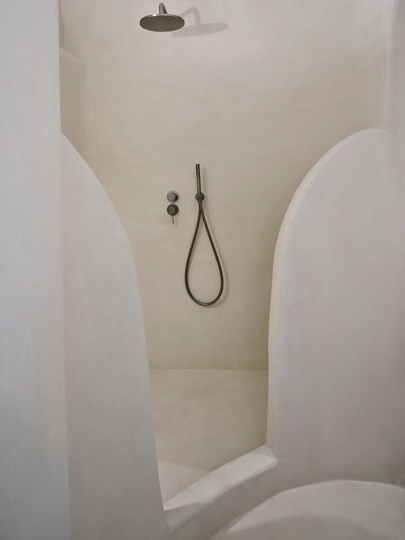 Minimalistische Dusche mit beigefarbenen Verputzwänden und dunkler Duscharmatur.