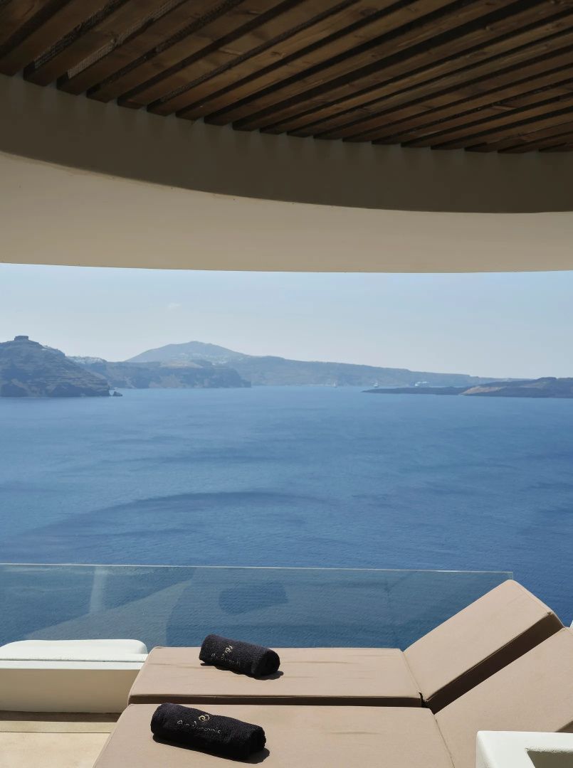 Blick von einer überdachten Terrasse auf das blaue Meer und die Vulkaninseln von Santorin.