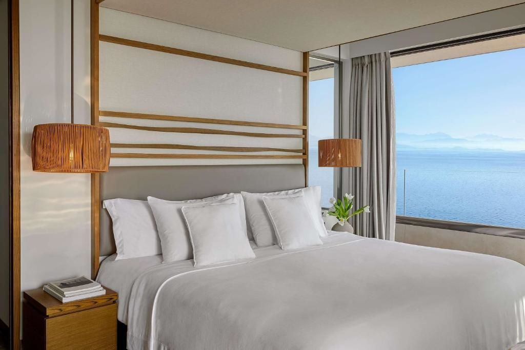 Doppelbett mit weißen Kissen und Holzdekoration mit Blick durch ein Fenster auf das Meer.