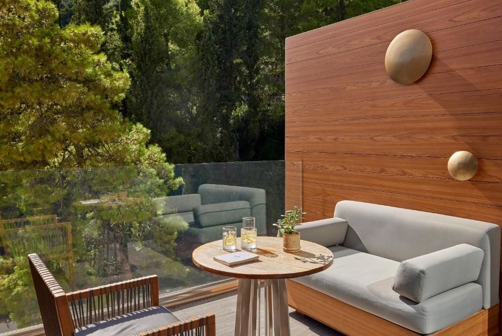 Balkon mit Holzverkleidung, gemütlicher Sitzcouch und Tisch vor grüner Baumkulisse.