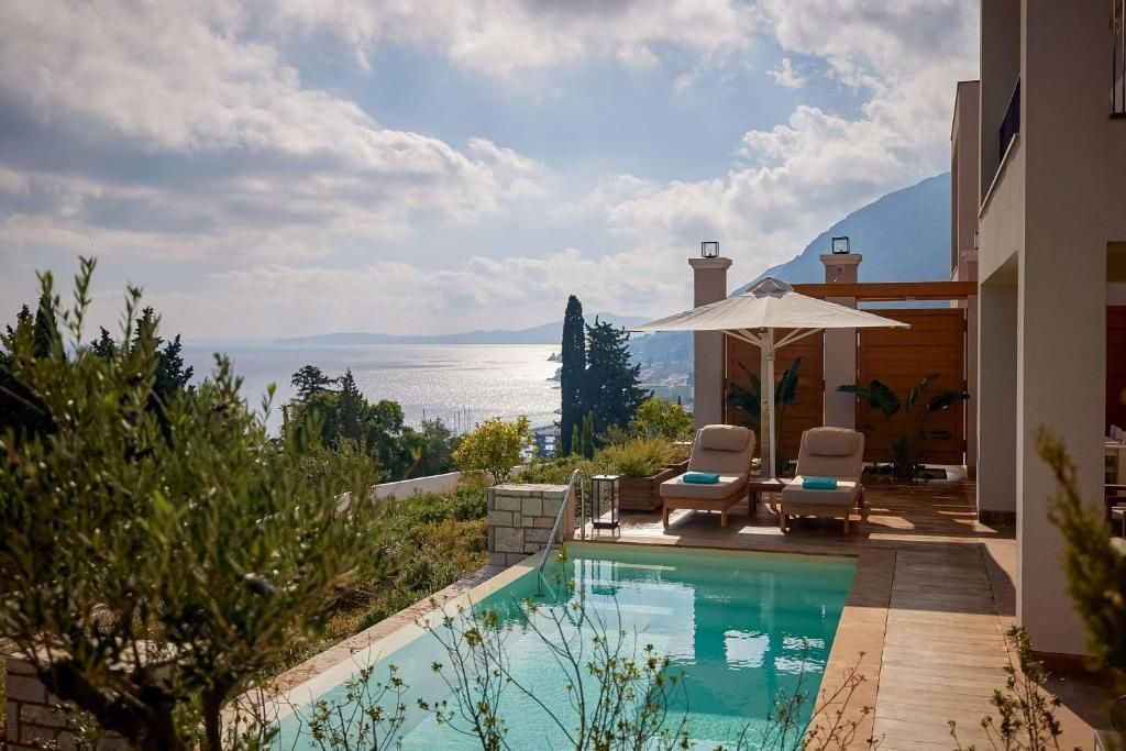 Sonnenterrasse mit privatem Pool, zwei Liegestühlen, Sonnenschirm und Blick auf das Meer und die Hügel.