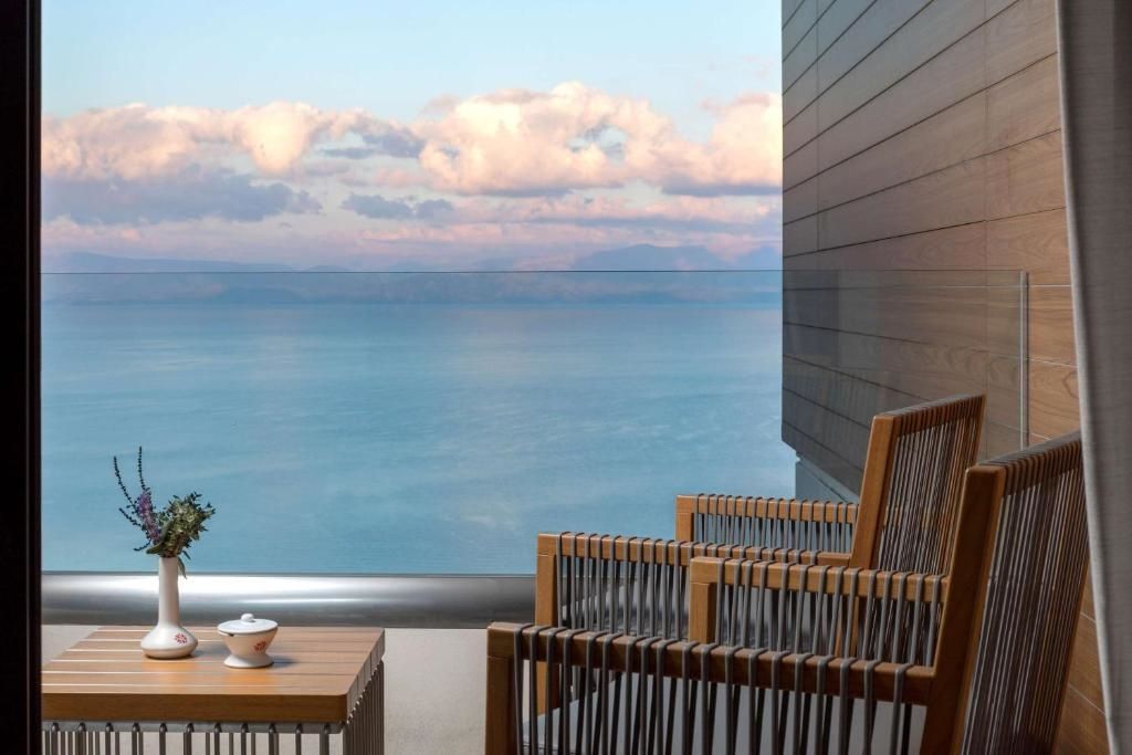 Balkon mit Holzstühlen und Blick auf das blaue Meer sowie den bewölkten Abendhimmel.