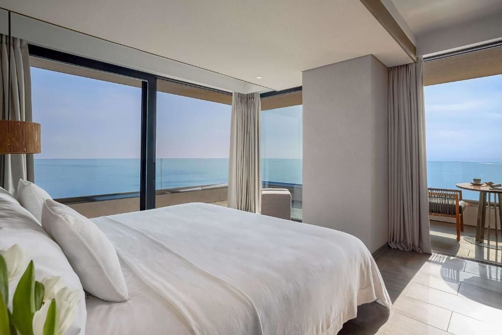 Helles Schlafzimmer mit großem Bett und bodentiefen Fenstern mit freiem Blick auf das Meer.