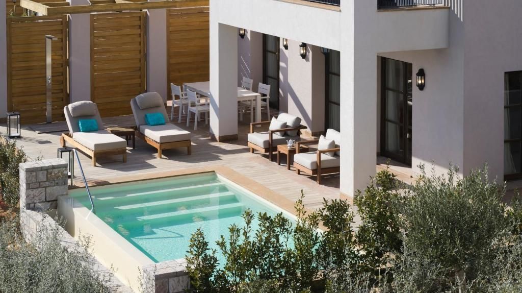 Terrassensitzbereich mit eigenem Pool, Sonnenliegen und Esstisch an einem hellen Gebäude.