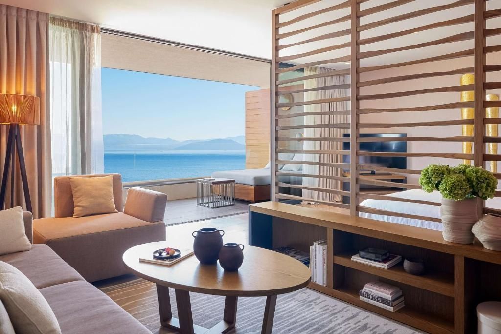 Sitzbereich einer Suite mit Sofa, Holztisch und großem Fenster zum Meer.