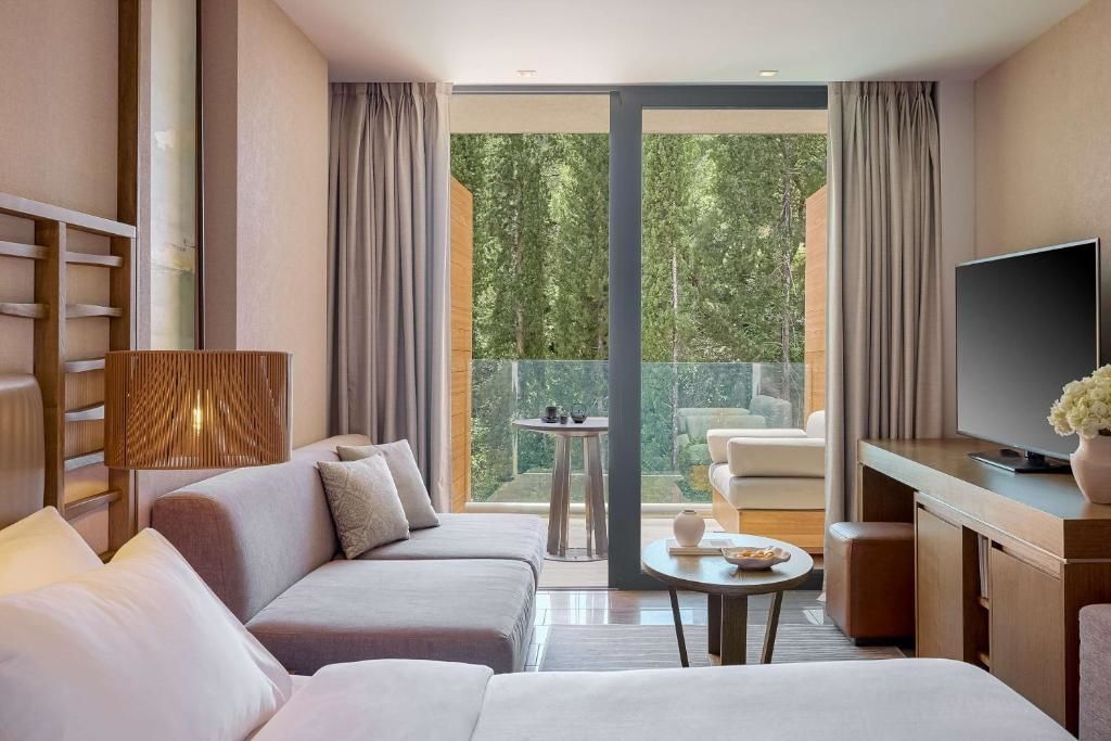 Sitzbereich in einem Hotelzimmer mit modernem Sofa und Blick auf den bewaldeten Balkon.
