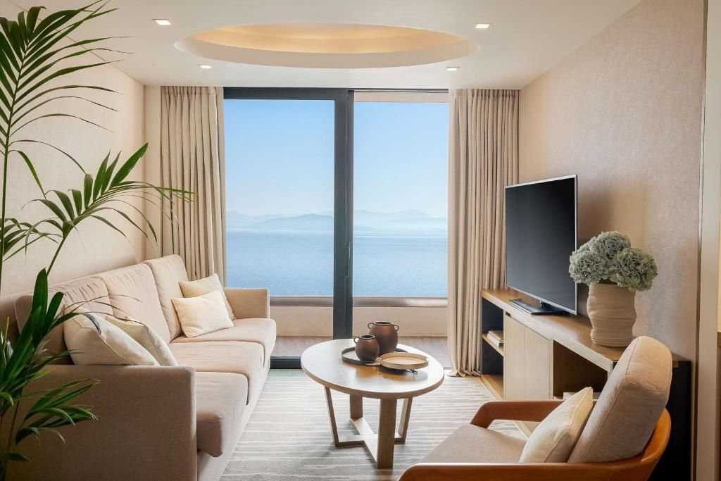 Wohnzimmer mit beigefarbenem Sofa, Couchtisch, Fernseher und Meerblick durch große Balkontüren.
