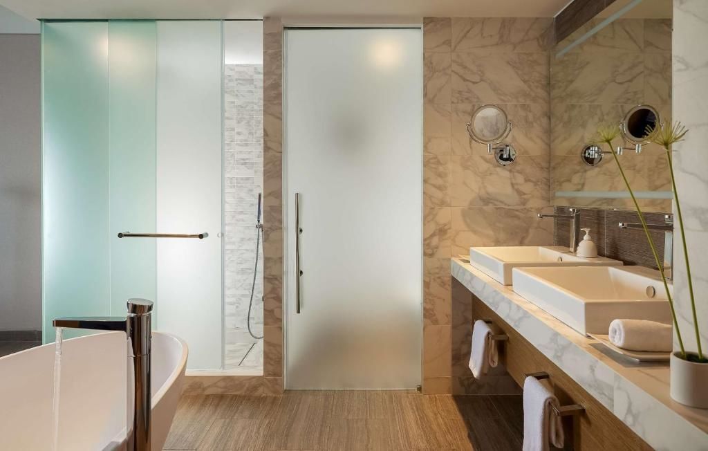 Badezimmer mit zwei Waschbecken auf einem Holzwaschtisch und Glasdusche.