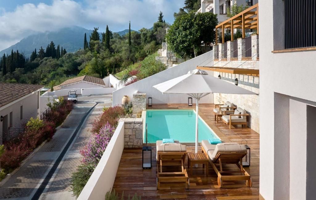 Terrasse mit Holzdeck, eigenem Swimmingpool, Sonnenschirm und Liegestühlen vor bewaldetem Hang.