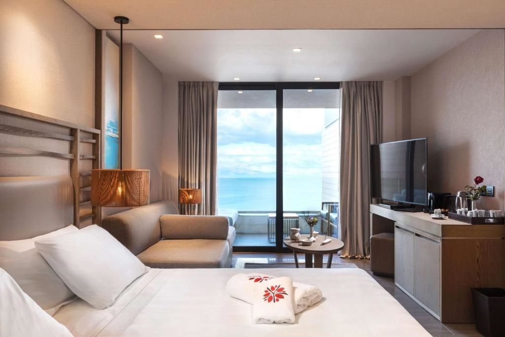 Hotelzimmer mit Blick vom Bett auf Sofa, Fernseher und den Balkon am Meer