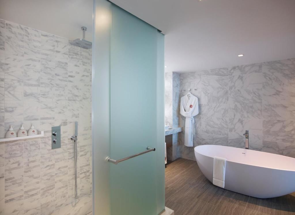 Badezimmer mit weißer freistehender Badewanne, Glasdusche und Bademantel an der Wand.