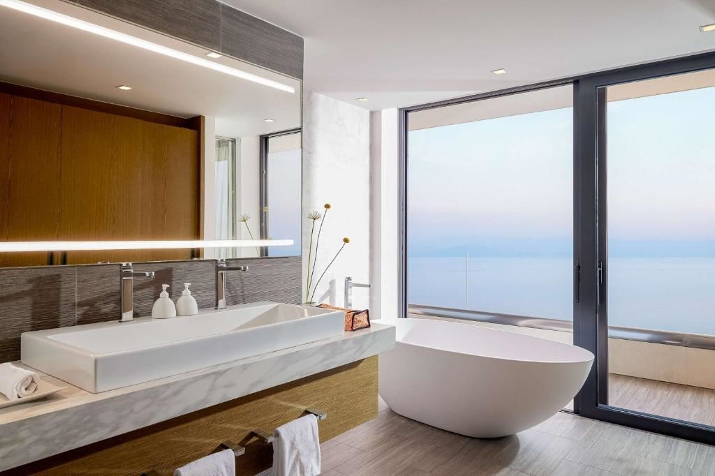 Badezimmer mit weißer freistehender Badewanne, Doppelwaschtisch und Aussicht auf das Meer.