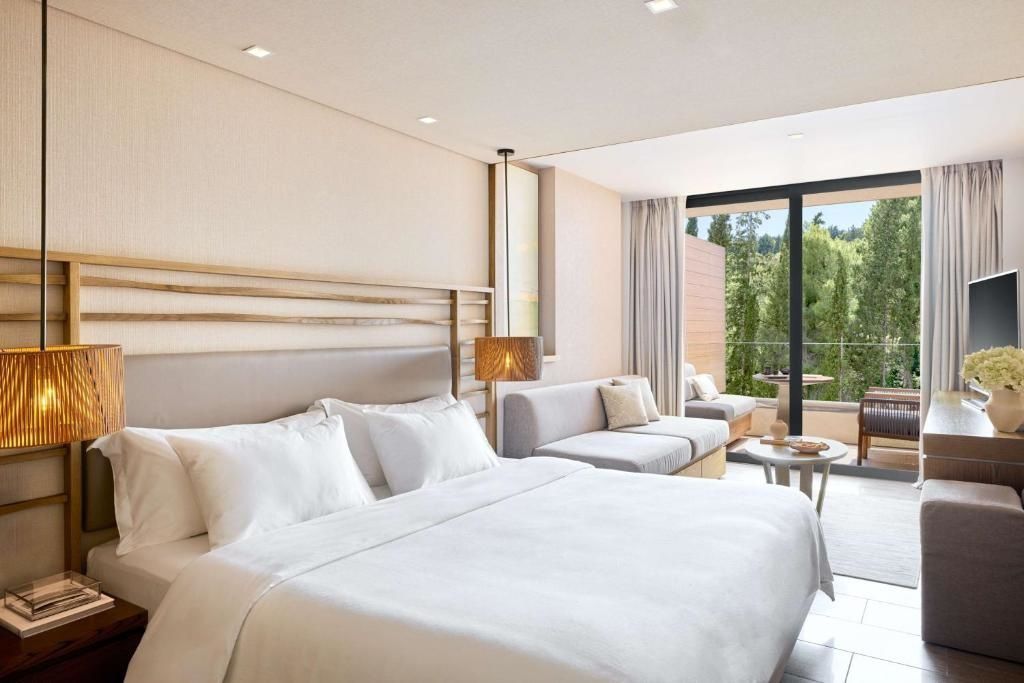 Helles Hotelzimmer mit großem Doppelbett, gemütlicher Couch und Zugang zum Balkon.