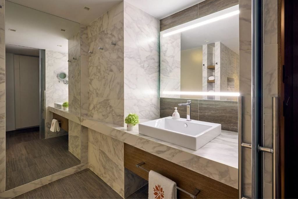 Badezimmer mit rechtekigem Aufsatzwaschbecken, großem beleuchtetem Spiegel und Marmorwand.