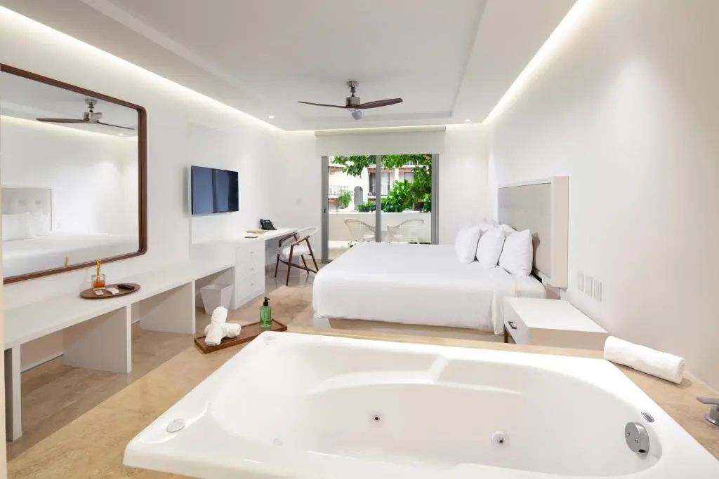 Helles Hotelzimmer mit großem Doppelbett, Schreibtisch und einem Whirlpool im Raum.