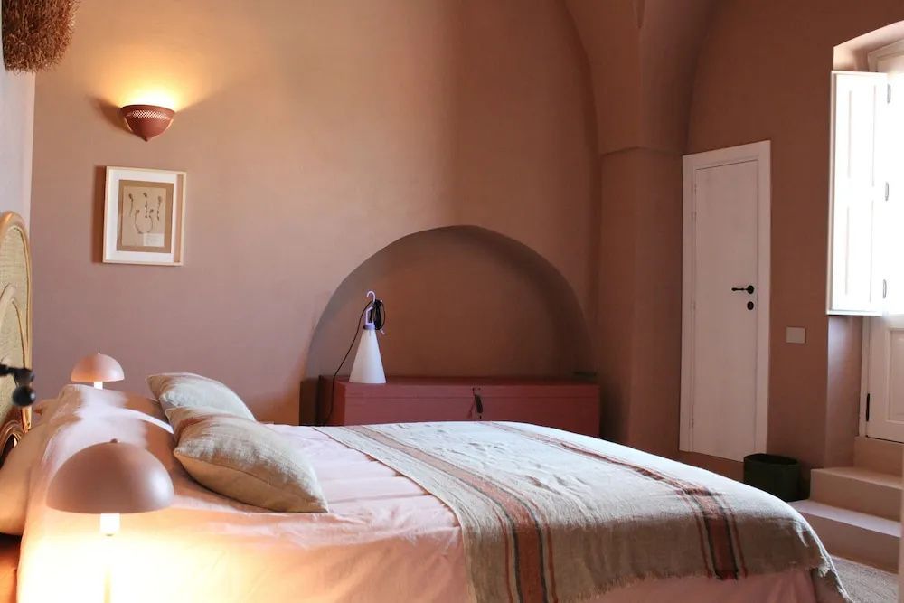 Schlafzimmer mit gewölbter Decke, terrakottafarbenen Wänden und einem gemachten Doppelbett.