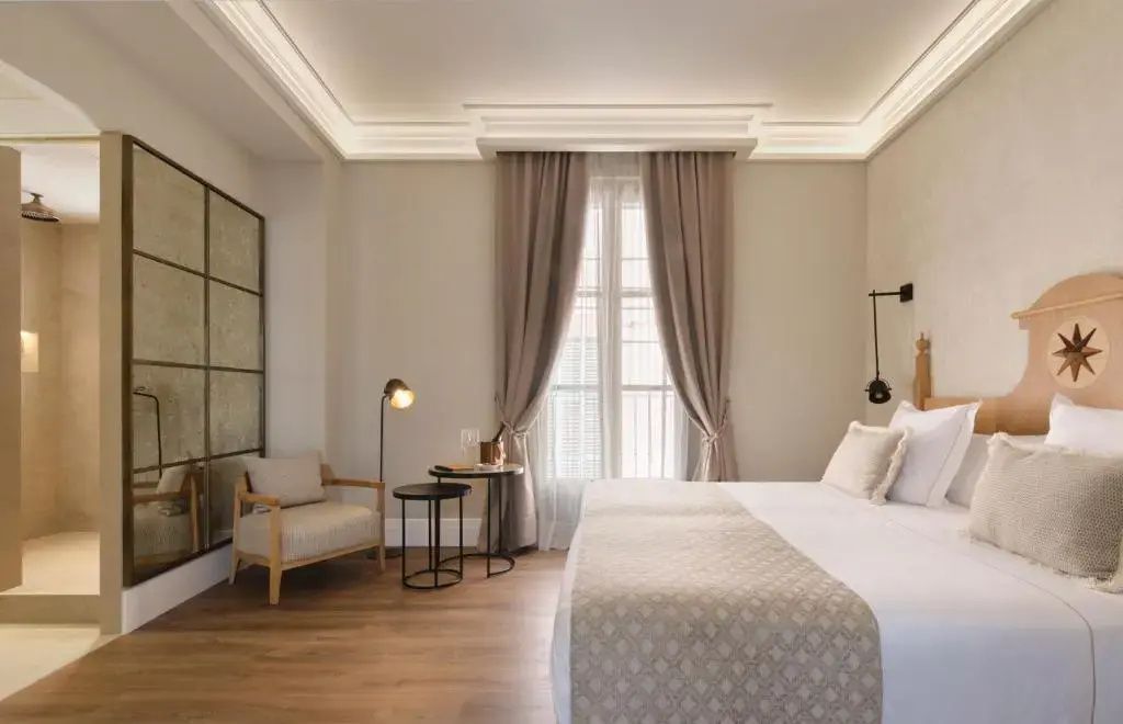 Schlafzimmer im Hotel mit Doppelbett, bodentiefem Fenster, Stehlampe und Sessel