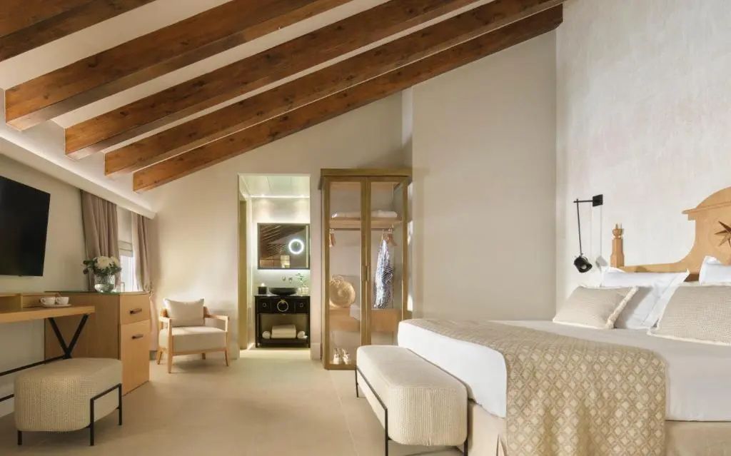 Hotelzimmer mit Holzbalkendecke, Doppelbett, transparentem Schrank und Blick ins Bad