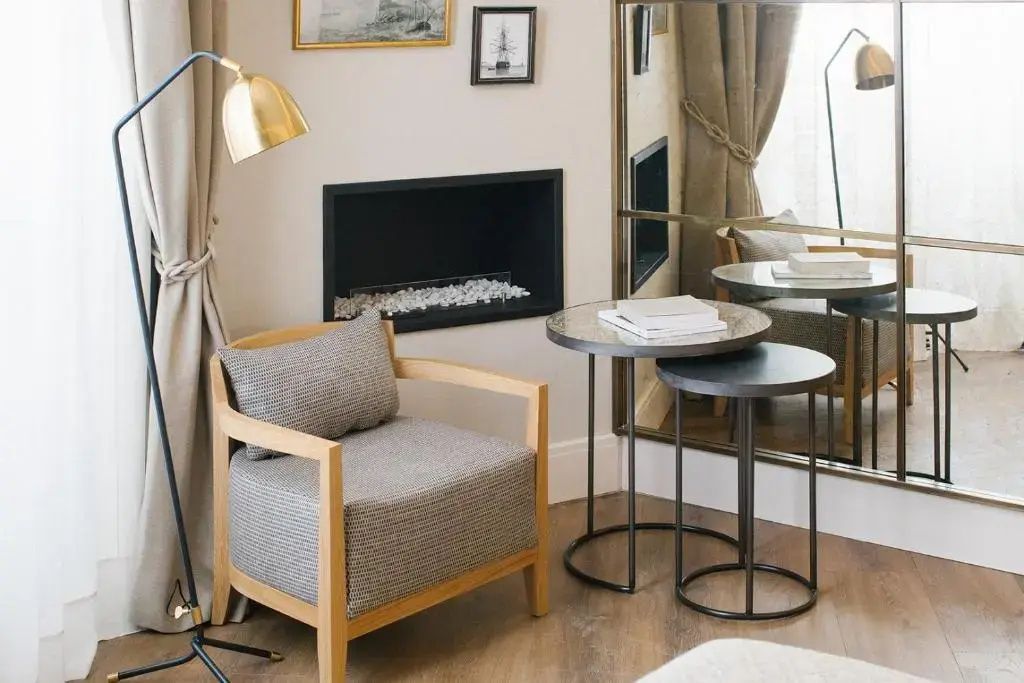 Sitzecke im Hotelzimmer mit grauem Sessel, Beistelltischen, Stehlampe und Kamin