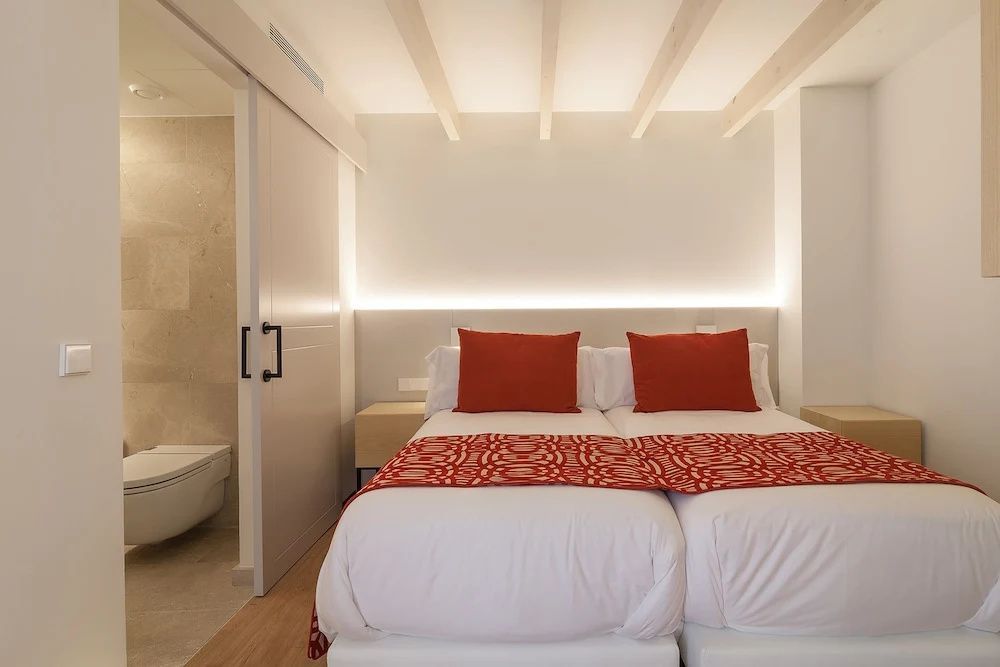 Helles Hotelzimmer mit Doppelbett, roten Kissen und Schiebetür zum Badezimmer.