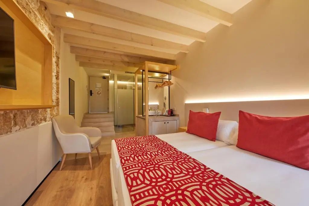 Blick auf das Doppelbett mit roter Tagesdecke und den Eingangsbereich der Suite mit Holzbalkendecke.