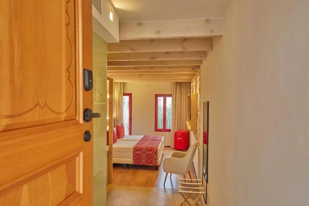 Blick durch die geöffnete Holztür in ein Hotelzimmer mit Doppelbett und Holzbalkendecke.
