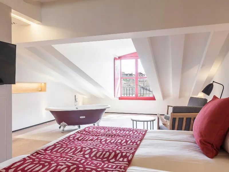 Freistehende rote Badewanne in einer Suite unter einer Dachschräge mit Fenster.