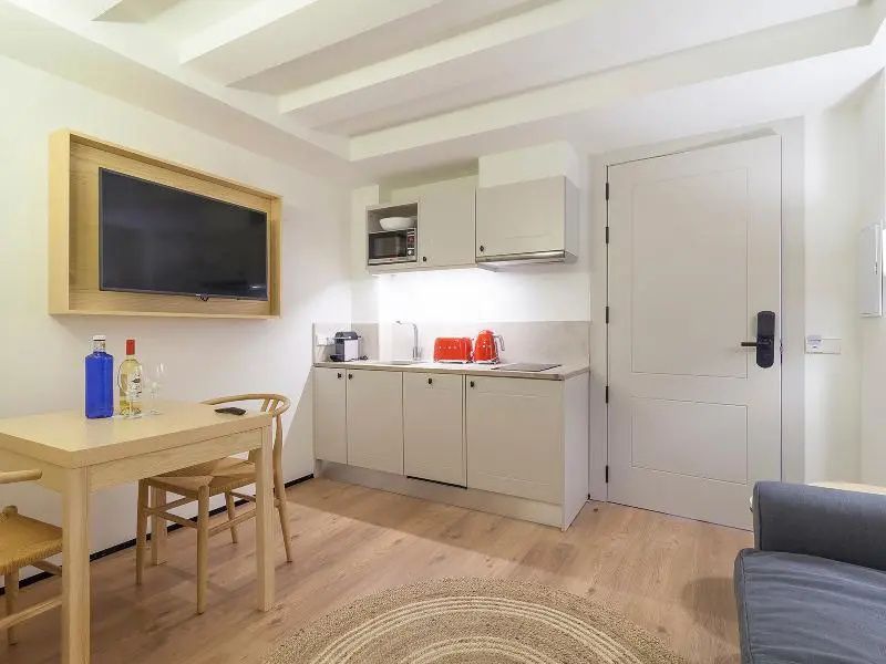 Helle Küchenzeile im Apartment mit Mikrowelle, rotem Toaster, Esstisch und Fernseher.
