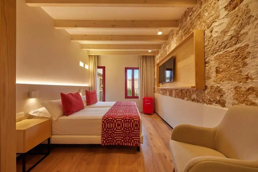 Hotelzimmer mit Doppelbett, Natursteinwand, Fernseher an der Wand und Holzbalkendecke.