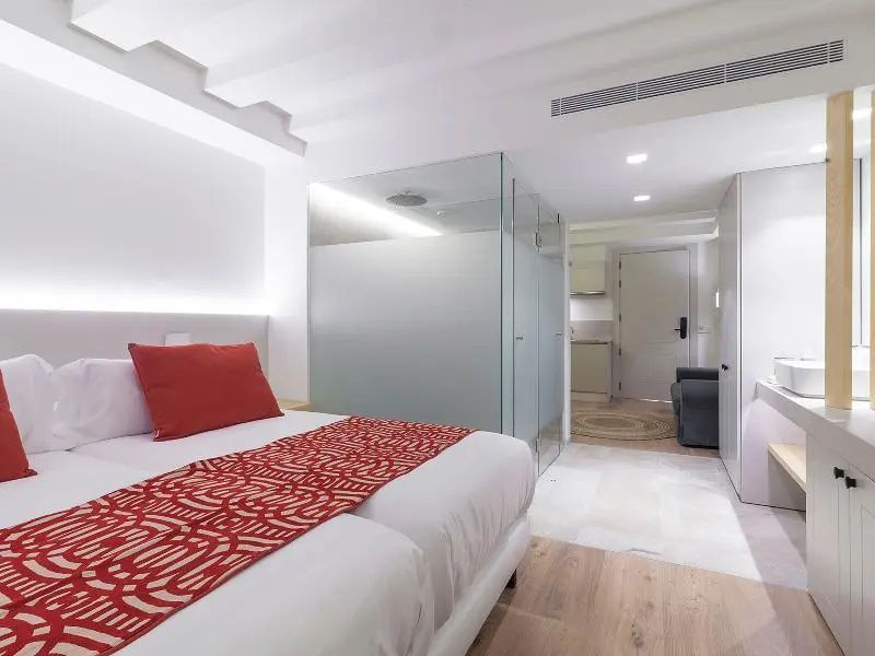 Schlafbereich mit Doppelbett und integrierter Glasduschkabine im hell eingerichteten Zimmer.