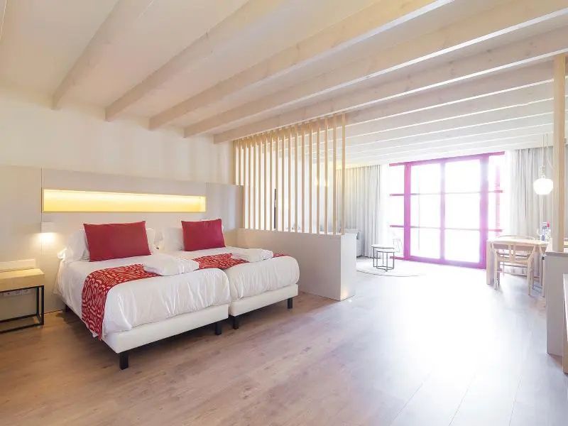Großzügiges Zimmer mit Holzbalkendecke, Doppelbett und rotem Fensterrahmen.