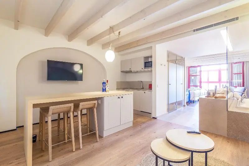Helle Suite mit offener Küchenzeile, Esstheke aus Holz und Wandfernseher.