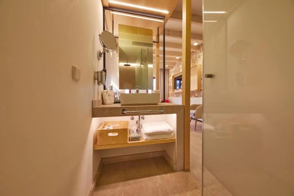 Moderner Waschplatz mit Aufsatzwaschbecken, Spiegel, Handtüchern und Holzregalen im Hotelzimmer.