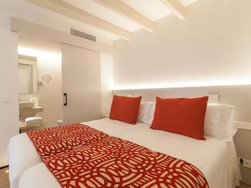 Doppelbett mit rot gemusterter Decke und Kissen vor einer weißen Schiebetür.