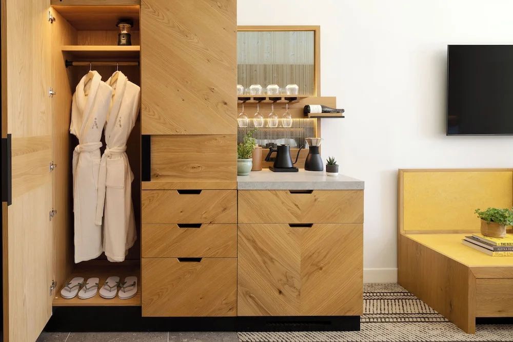Ein moderner Holzschrank im Hotelzimmer mit aufgehängten Bademänteln, Hausschuhen und Kaffeestation.