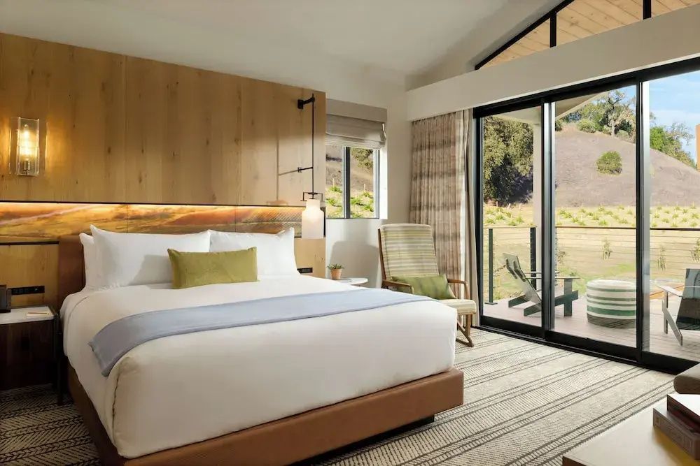 Helles Hotelzimmer mit Doppelbett, Holzverkleidung und Schiebetür zum Balkon.