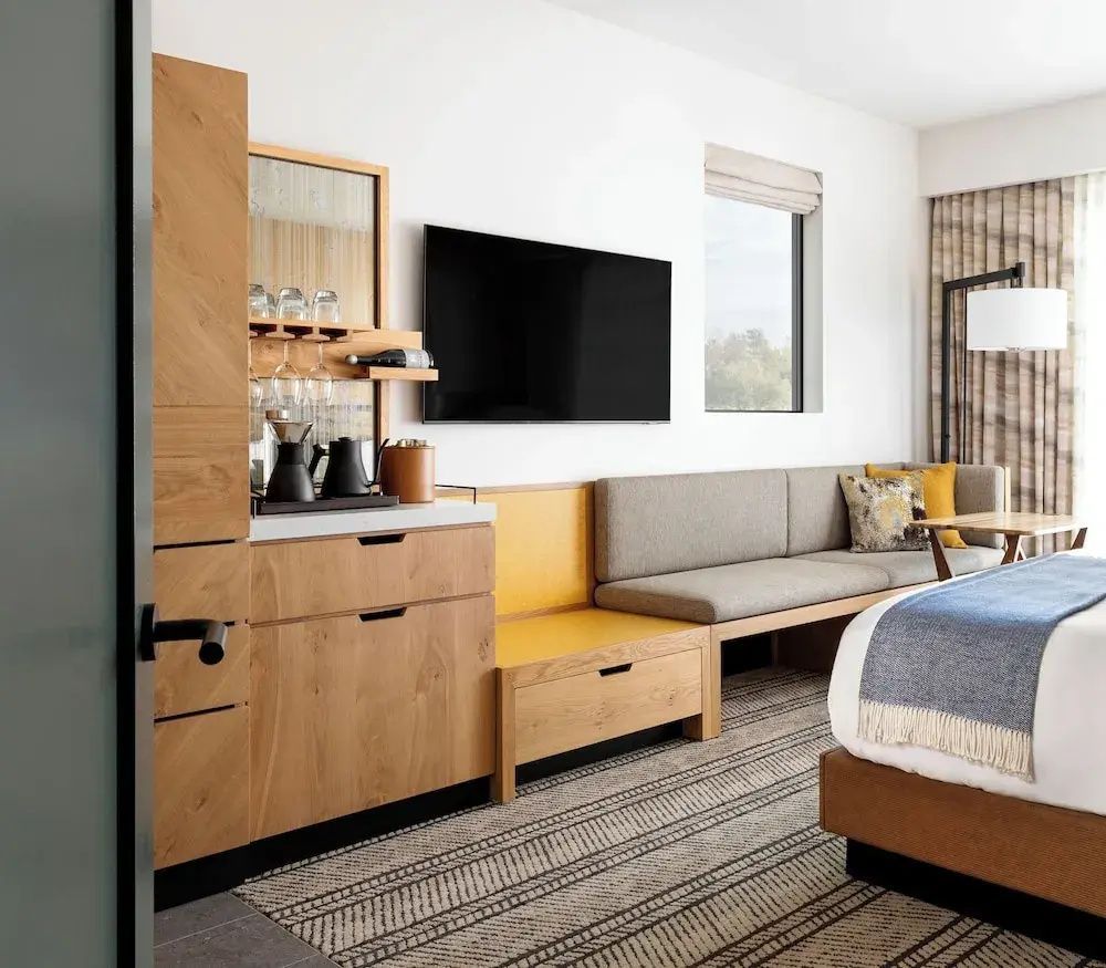Modernes Hotelzimmer mit Holzmöbeln, Sitzbank, Fernseher an der Wand und Kaffeestation.