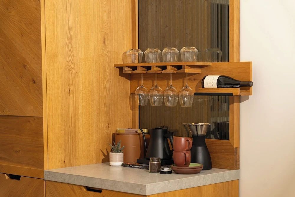 Kaffeestation mit Weinflasche, Gläserregal, Wasserkocher und Tassen auf einer Arbeitsplatte aus Stein.