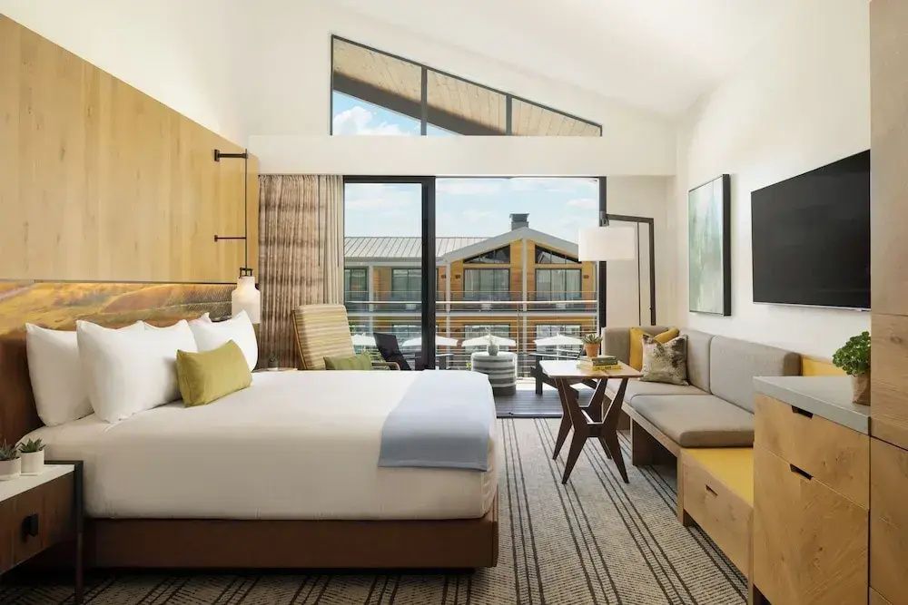 Helles Zimmer mit Doppelbett, Balkonfenster, Sitzbereich und hoher Decke.