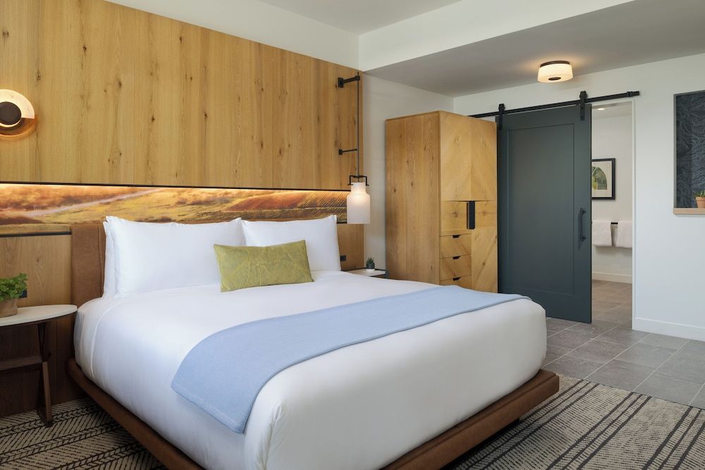 Doppelbett mit weißer Bettwäsche, Holzverkleidung, blauem Läufer und Holzschrank.