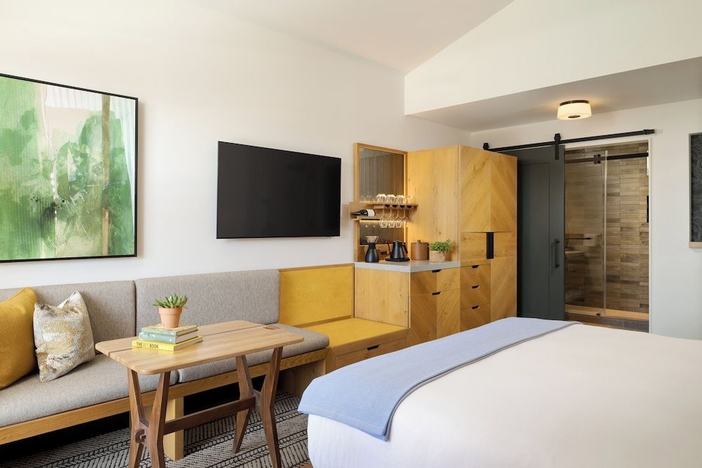 Hotelzimmer mit hellem Doppelbett, Fernseher an der Wand, Holzmöbeln und einer integrierten Sitzbank.