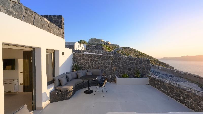 Terrassenbereich mit dunkler Ecksitzbank, kleinem Tisch und Natursteinmauer an einer weißen Fassade.
