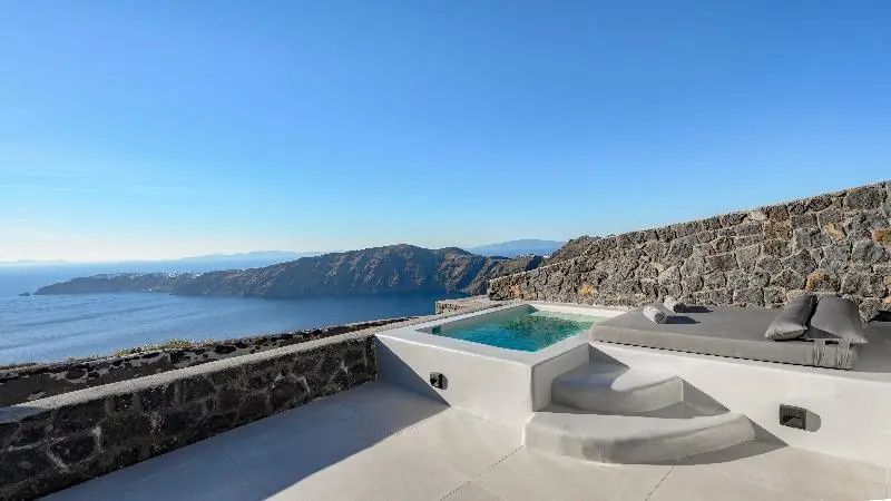 Terrasse mit Whirlpool und Blick auf das Meer und Felsen unter blauem Himmel.